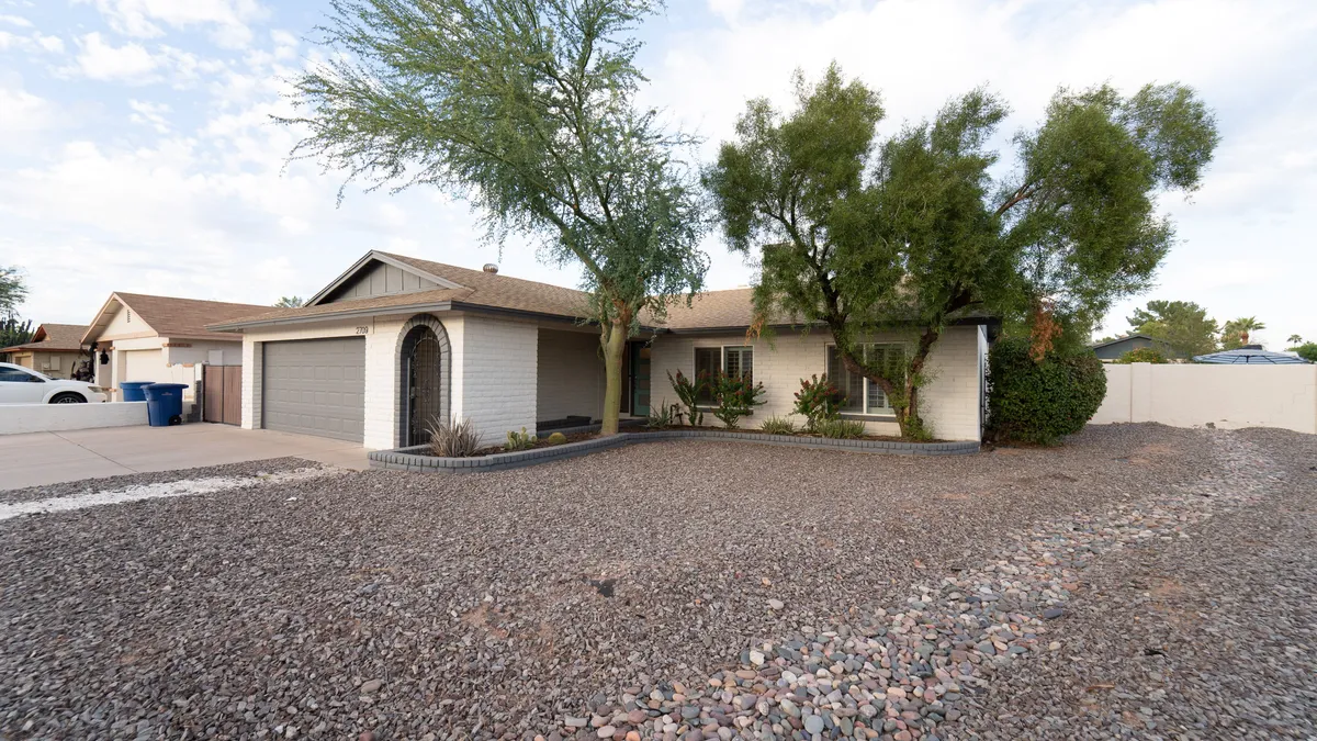 A welcoming front yard scene with green foliage, a landscaped entryway, and a rocky driveway leading up to the home’s exterior. The tranquil atmosphere highlights ease of access for pet owners and offers a glimpse of the neighborhood's peaceful vibe.