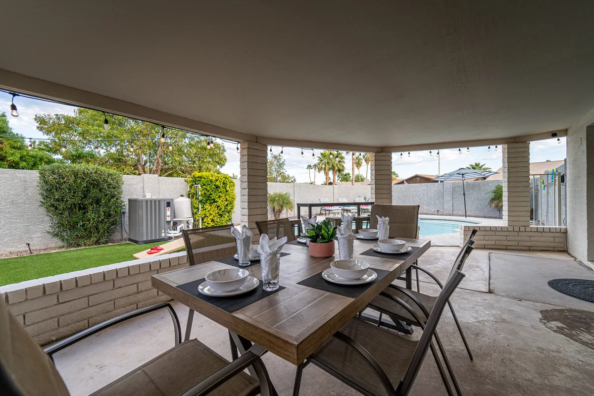 A dining table is elegantly set for a meal, with a sparkling swimming pool and verdant greenery visible in the background. The scene captures the spirit of outdoor dining and celebrates the seamless flow between leisure at home and the excitement found nearby.