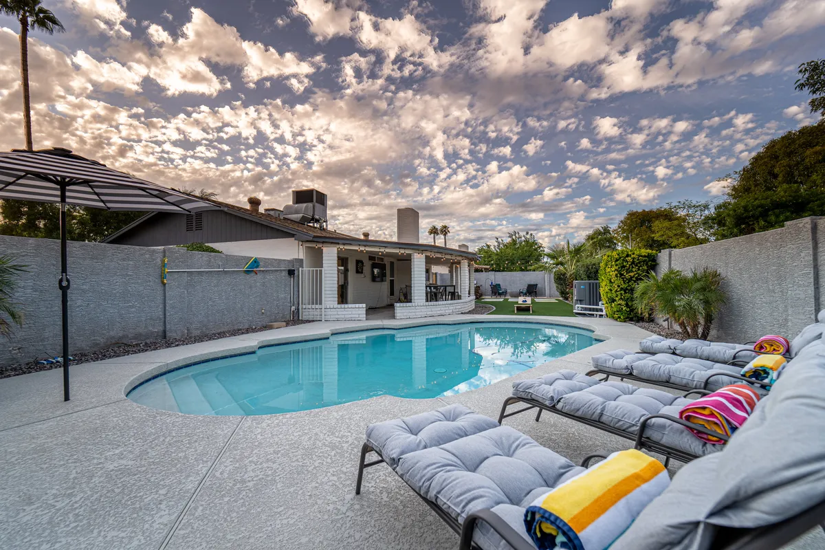 An inviting exterior scene highlighting a heated swimming pool surrounded by lounge chairs and a spacious patio area beneath a colorful, cloudy sky. The view suggests both daytime relaxation and serene evening swims, with the patio offering a seamless connection to the outdoors.
