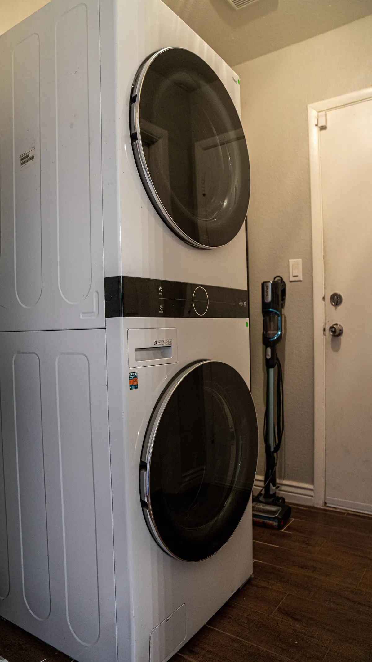 A utility area featuring a stacked washer and dryer, along with cleaning supplies neatly arranged. The scene is practical, organized, and highlights the convenience of having laundry amenities within easy reach.