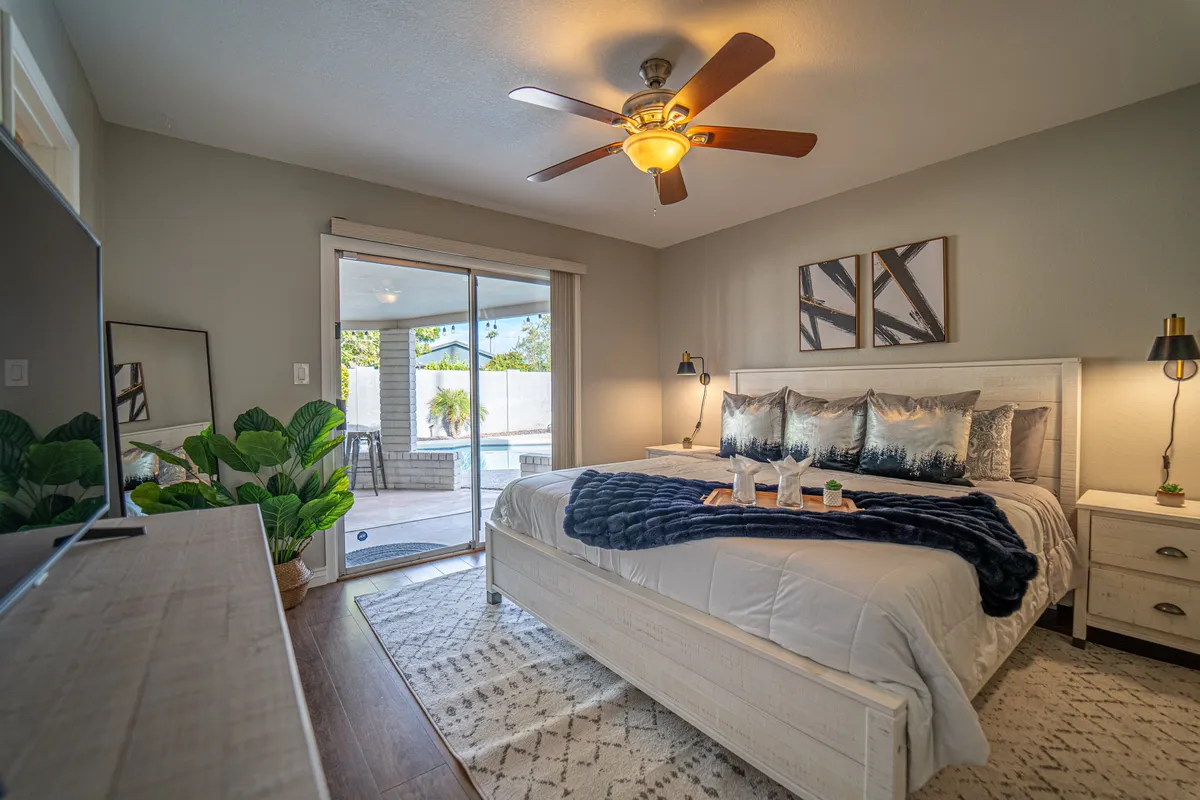 A tranquil bedroom with a plush bed adorned with decorative pillows, a nightstand with a lamp, and sliding glass doors that open directly to a pool area. Bright natural light filters in, and the view of the pool invites relaxation and easy access for a morning swim or moonlit dip.