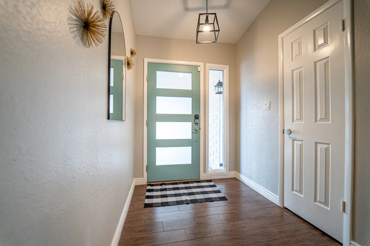 A welcoming entryway featuring a cheerful mint green front door, black and white checkered rug, decorative mirror, and a hanging lantern. The space exudes hospitality and sets a positive first impression as guests arrive.