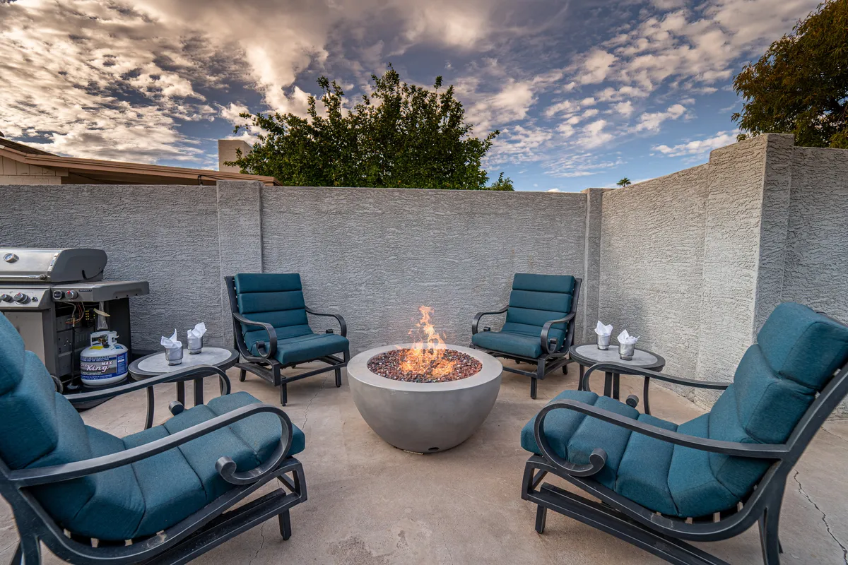 This cozy exterior shot highlights a fire pit with comfortable seating and a grill nearby, set against the backdrop of the evening sky. The space is perfect for winding down after a swim, sharing stories around the fire, or enjoying a romantic evening outdoors.