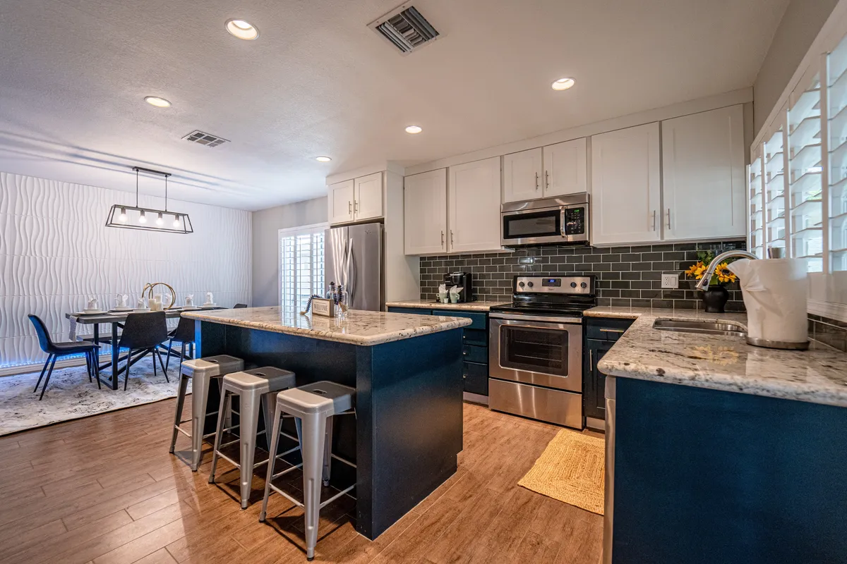 An inviting and modern kitchen area with a spacious kitchen island, a dining table set for six, and stainless steel appliances. The setup shows excellent space for cooking, dining, and socializing, with clean lines and contemporary finishes.