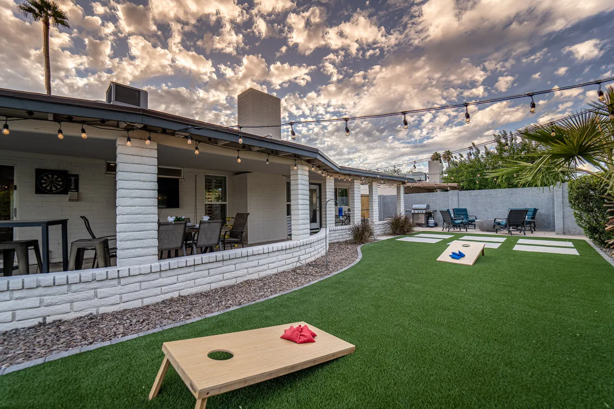 A vibrant outdoor area with a cornhole game setup, string lights overhead, a landscaped lawn, and a comfortable seating space. The festive mood and open space highlight opportunities for play, relaxation, and quality time with pets and family.