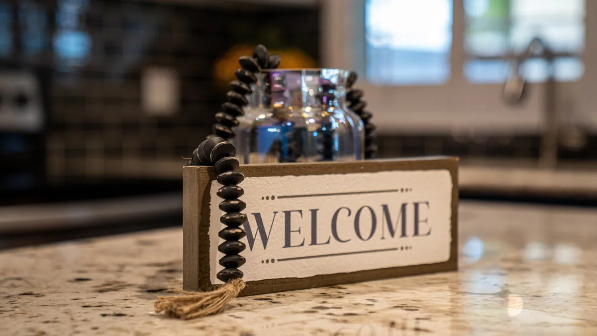 An interior setting with a welcome sign on a granite countertop, accompanied by a glass vase. The overall mood is warm and inviting, evoking hotel-style touches and a sense of being cared for upon arrival.