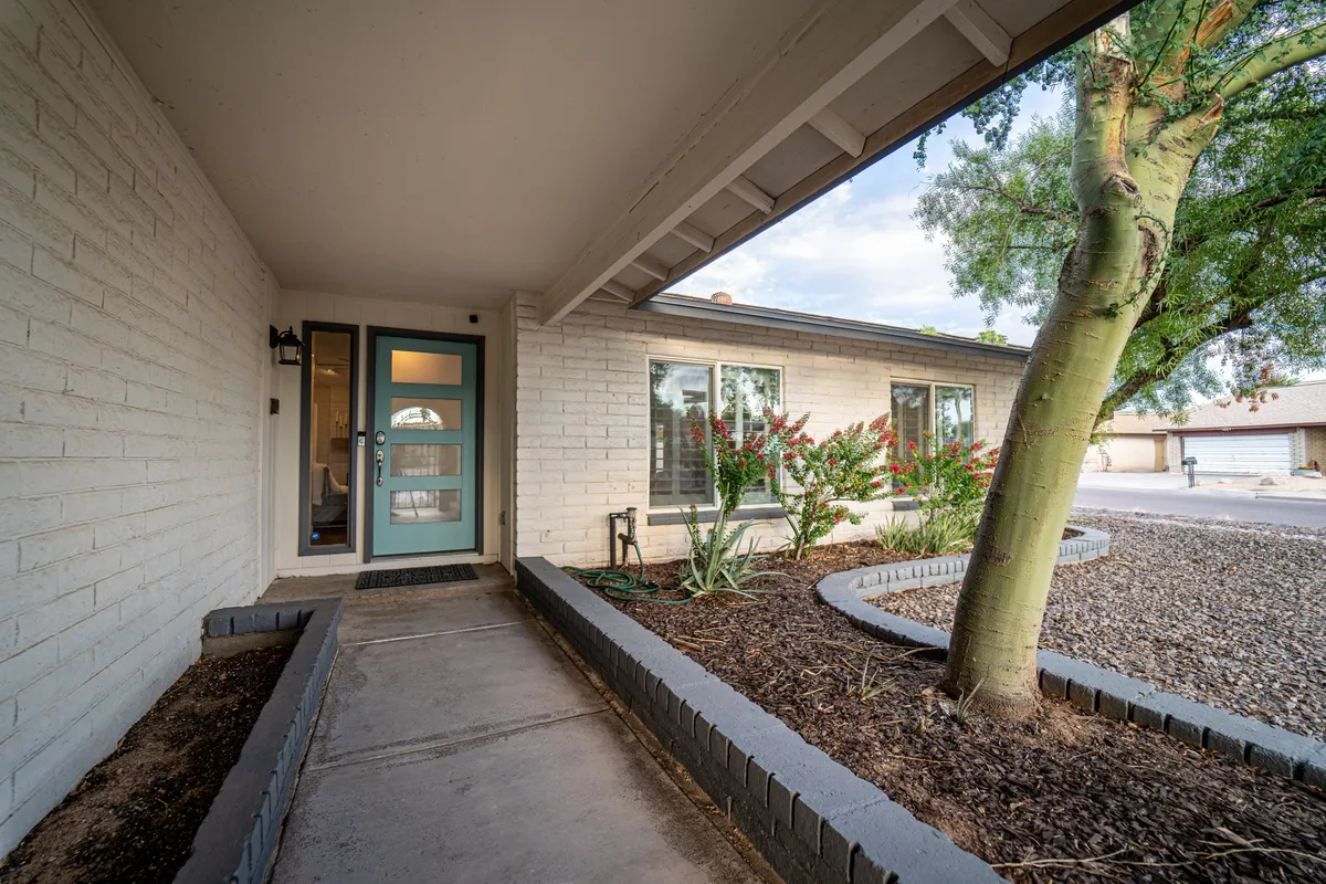 This image features the inviting front entryway of the property, complete with a well-maintained pathway, lush landscaping, and a welcoming door shaded by a leafy tree. The scene captures the sense of arrival and the property’s connection to its surroundings.